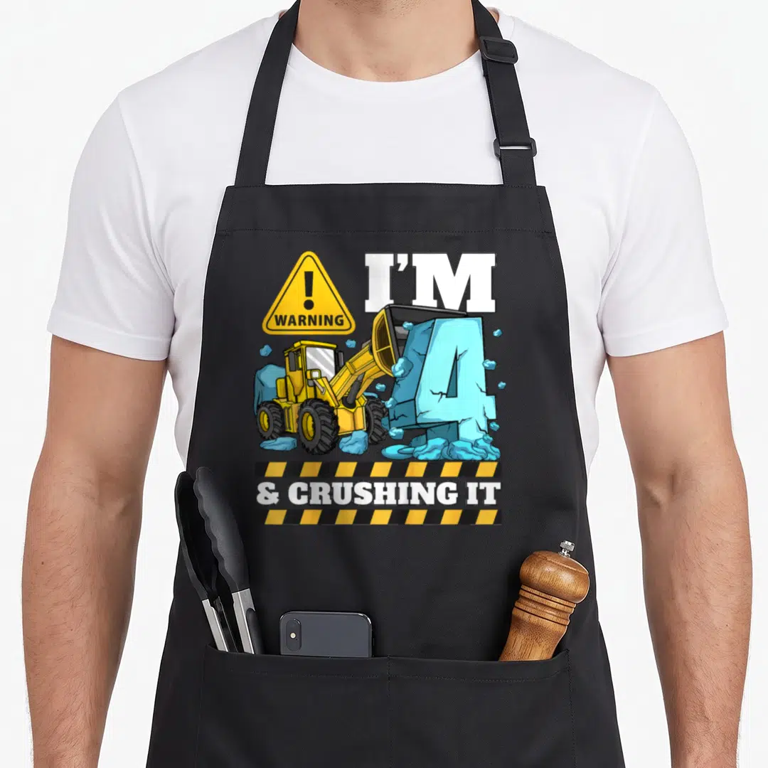 Bulldozer digger truck apron - Cartoon front loader pushing blue number four with warning sign and hazard stripes — shown on a black cotton canvas apron against a white background
