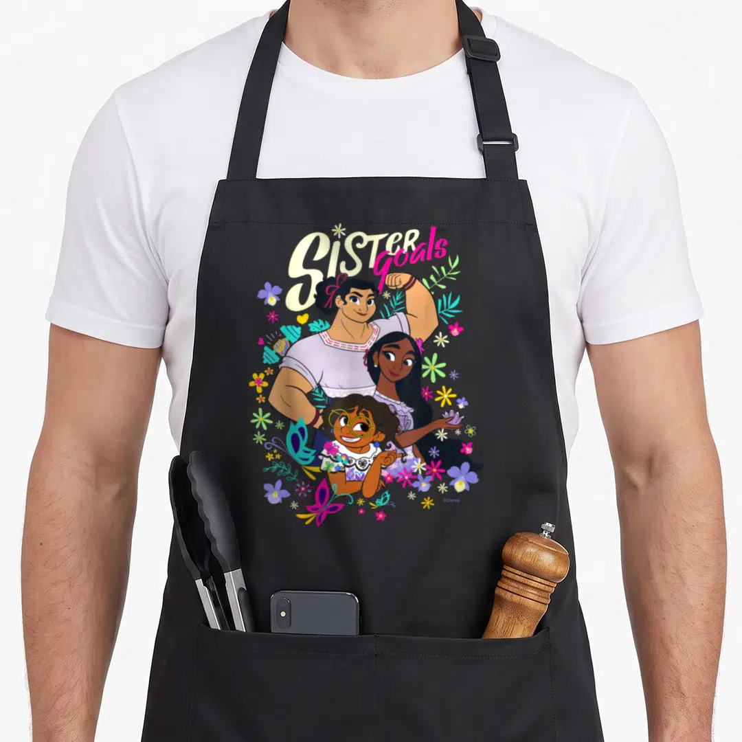 Mirabel sister goals apron - Three sisters stacked vertically under arched Sister goals text with purple, yellow, pink — shown on a black cotton canvas apron against a white background