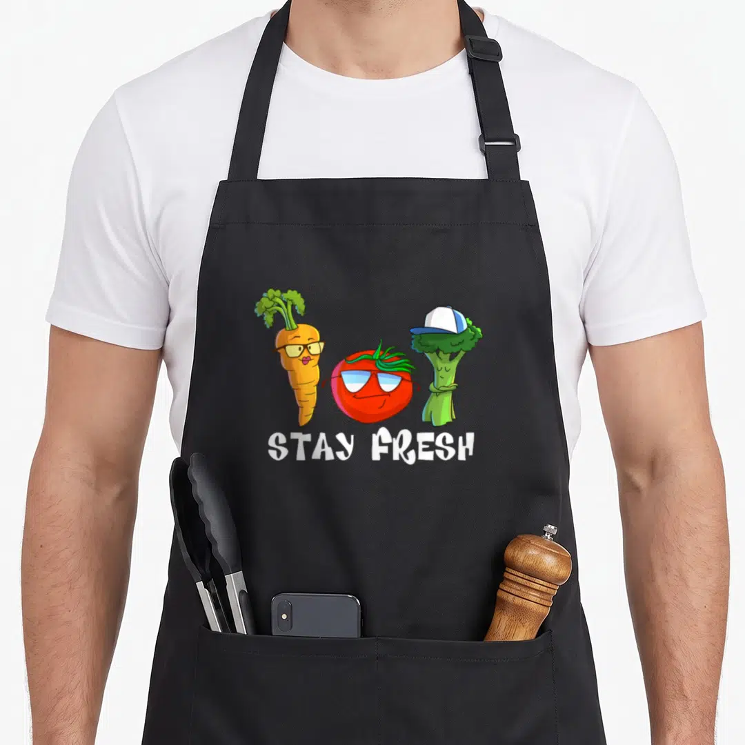Lunch vegetable apron - Three cartoon vegetables with glasses and cap above white STAY FRESH text — shown on a black cotton canvas apron against a white background