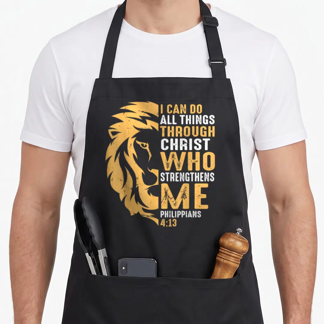 Through funny christian aprons - Yellow and white distressed lion profile next to stacked Bible verse text — shown on a black cotton canvas apron against a white background