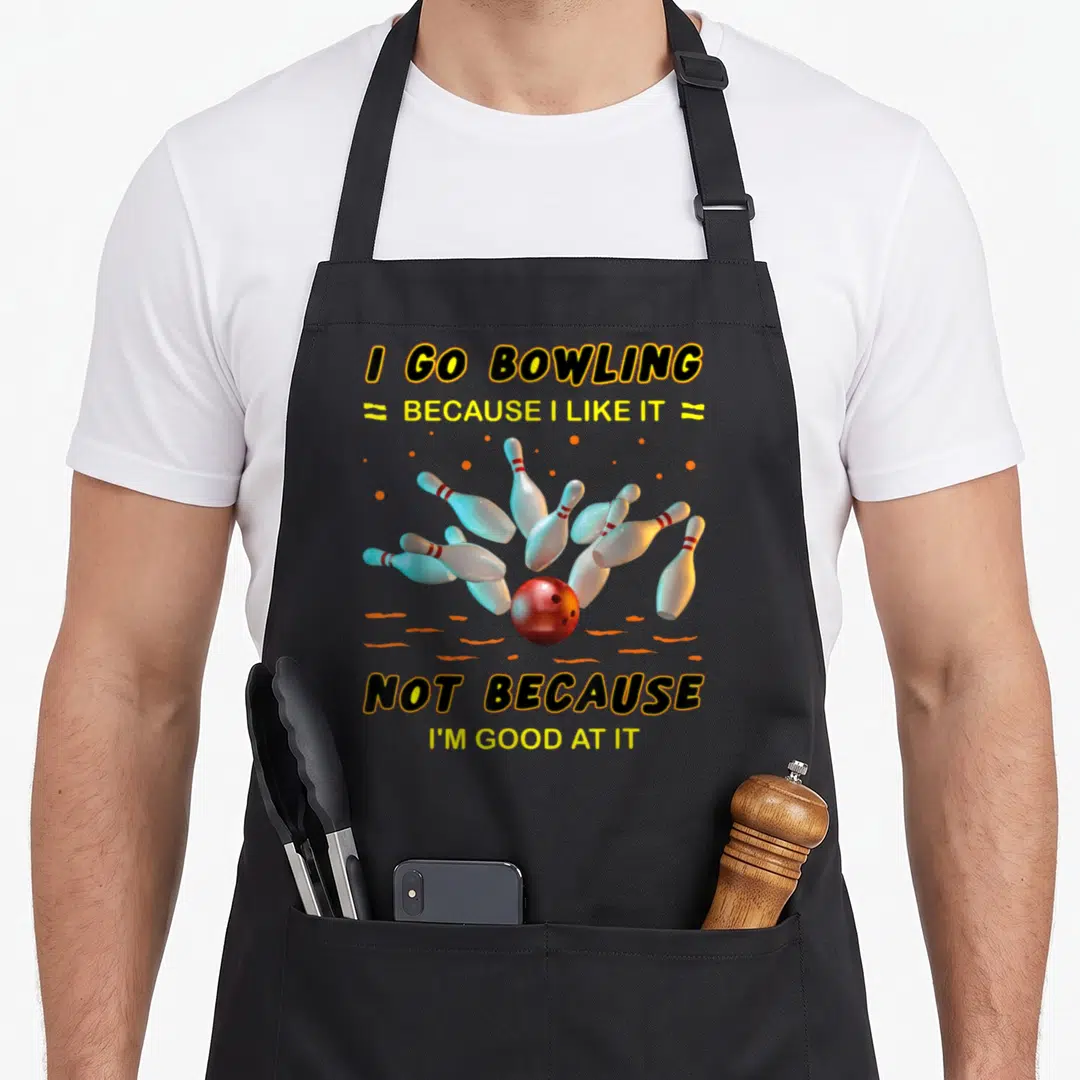 Bowling novelty apron - Red bowling ball hitting white pins with humorous quote about liking the sport not skill — shown on a black cotton canvas apron against a white background