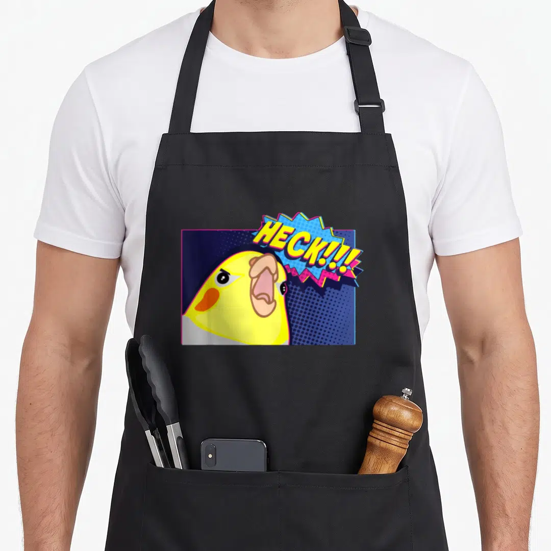 Heck meme apron - Cartoon yellow cockatiel head with open mouth next to blue and pink speech bubble reading HECK!!! — shown on a black cotton canvas apron against a white background