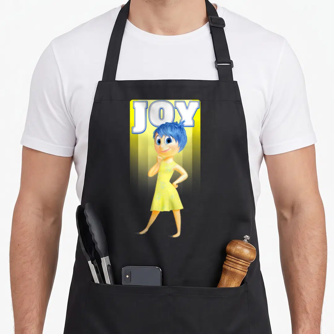 Joy sunny apron - Cartoon blue-haired character on yellow background with white JOY text outlined in blue — shown on a black cotton canvas apron against a white background