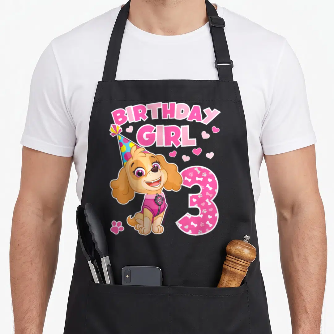 Merchandise birthday apron - Cartoon dog with party hat, BIRTHDAY GIRL text, and patterned number 3 — shown on a black cotton canvas apron against a white background