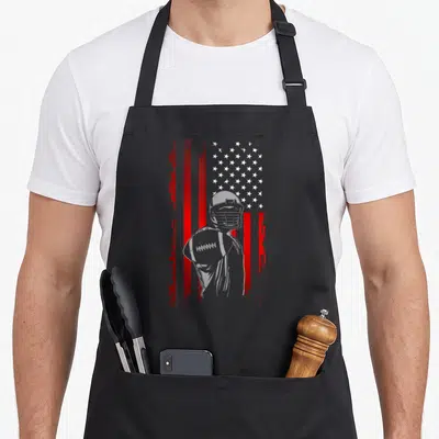 Retro football apron - Grey football player silhouette holding ball over distressed red and white striped flag — shown on a black cotton canvas apron against a white background
