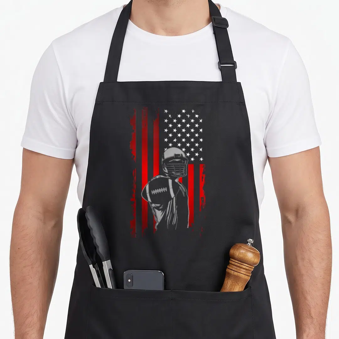 Retro football apron - Grey football player silhouette holding ball over distressed red and white striped flag — shown on a black cotton canvas apron against a white background