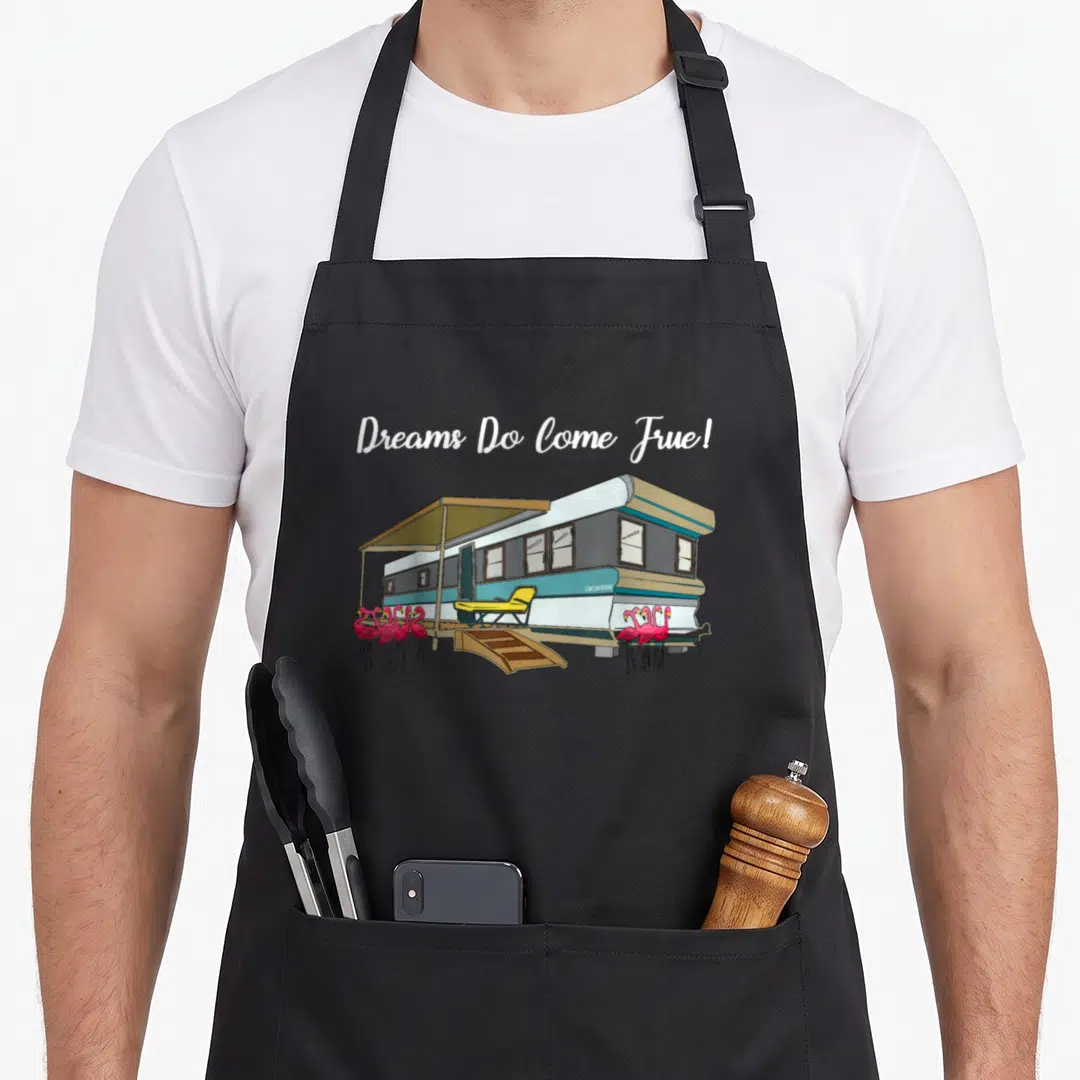 Flamingo trailer apron - Cartoon trailer with pink flamingos and Dreams Do Come True text — shown on a black cotton canvas apron against a white background
