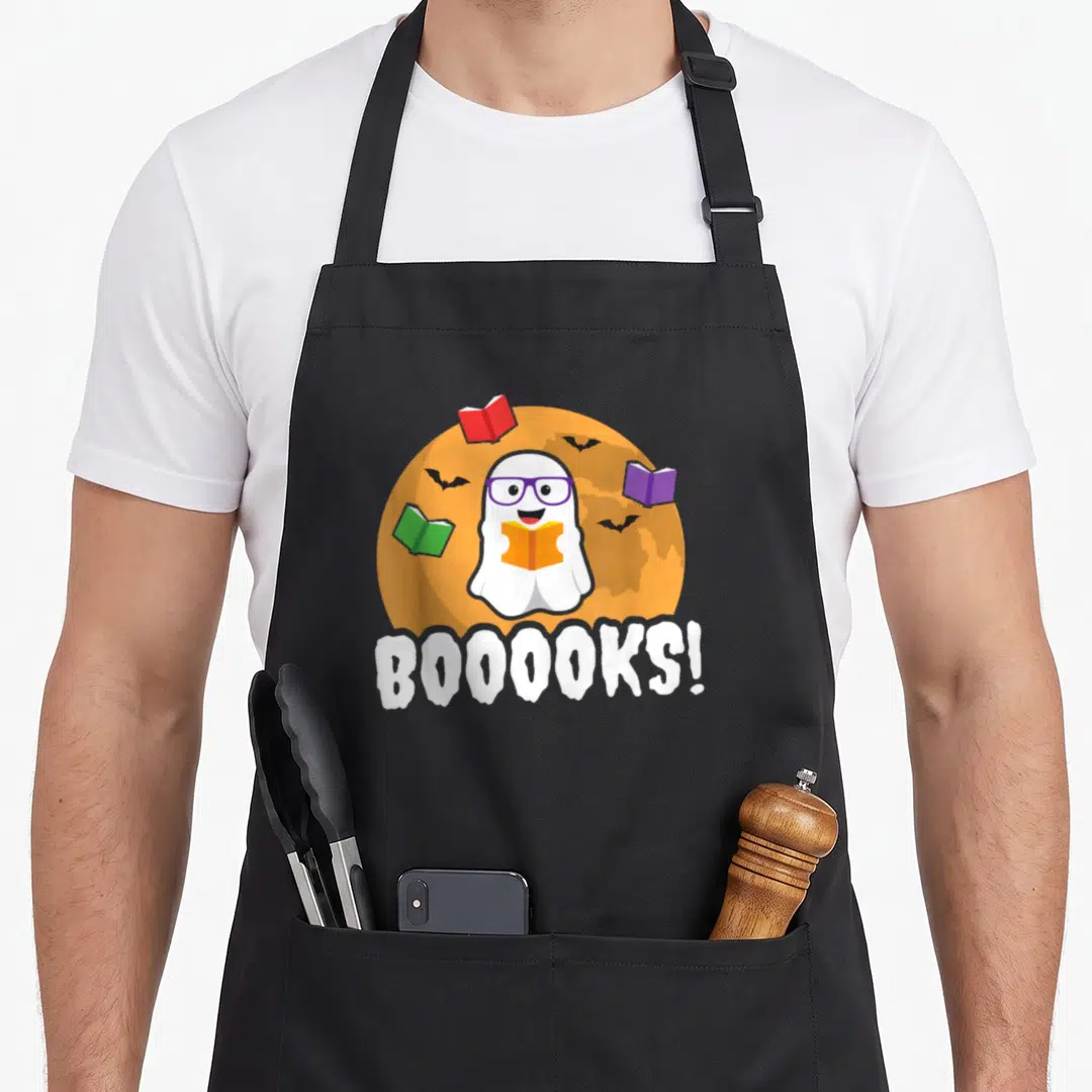 Booook ghost apron - Cartoon ghost with purple glasses holding book before orange moon with floating books and BOOOOKS — shown on a black cotton canvas apron against a white background