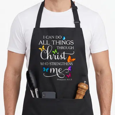 Through butterfly apron - I can do all things through Christ who strengthens me with six colorful butterflies stacked — shown on a black cotton canvas apron against a white background