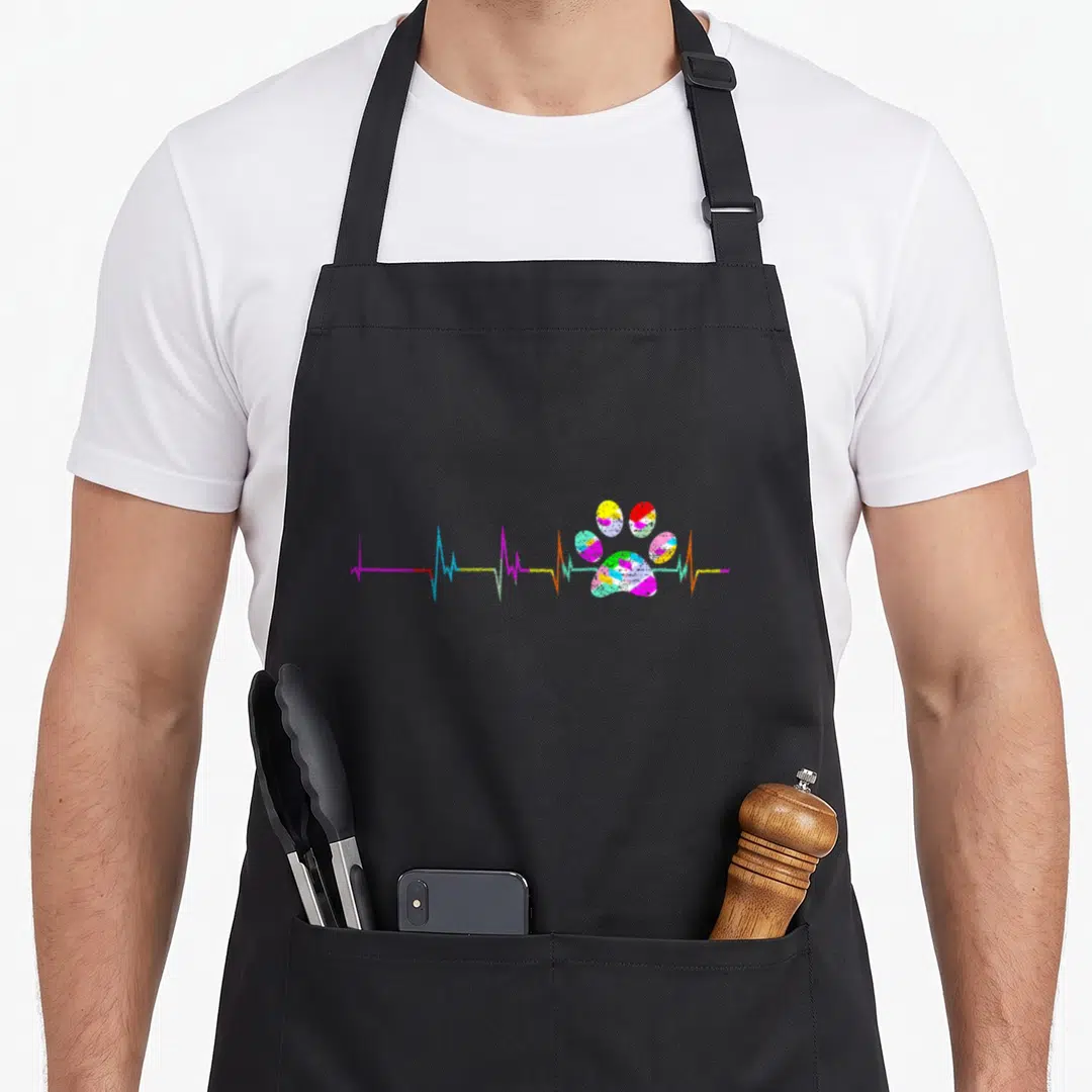 Retro dog paw print apron - Multicolored heartbeat line with segmented paw print in pink blue yellow green red — shown on a black cotton canvas apron against a white background