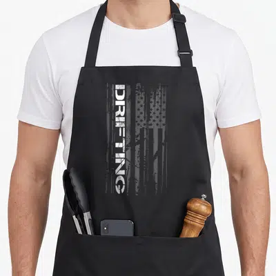 Car racing american flag apron - Vertical DRIFTING text over distressed white and grey USA flag graphic — shown on a black cotton canvas apron against a white background