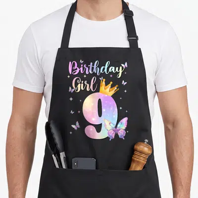 Theme butterfly aprons - Birthday Girl 9 with crown, butterflies, stars in purple pink yellow blue cartoon art — shown on a black cotton canvas apron against a white background