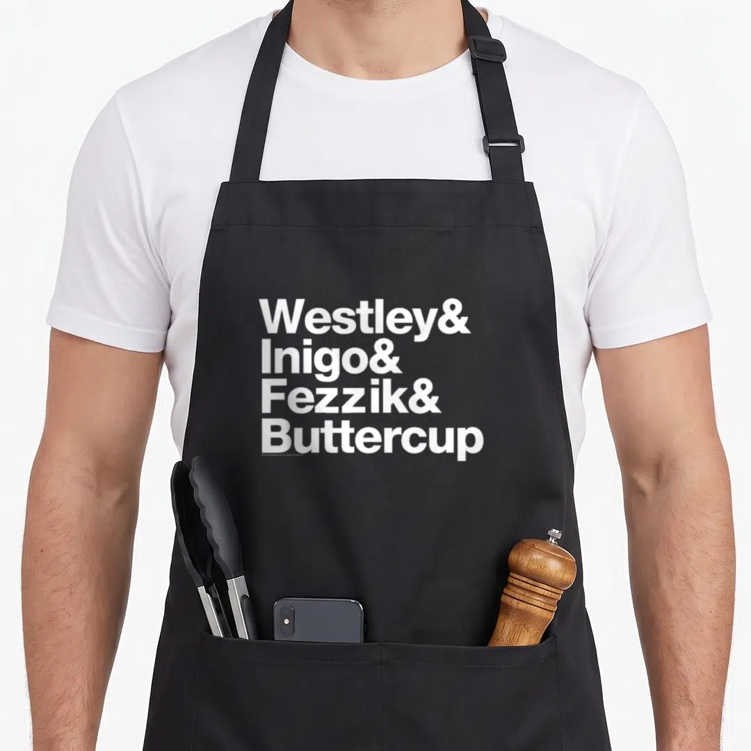 Westley princess apron - Stacked white text listing Westley, Inigo, Fezzik, and Buttercup with ampersands — shown on a black cotton canvas apron against a white background