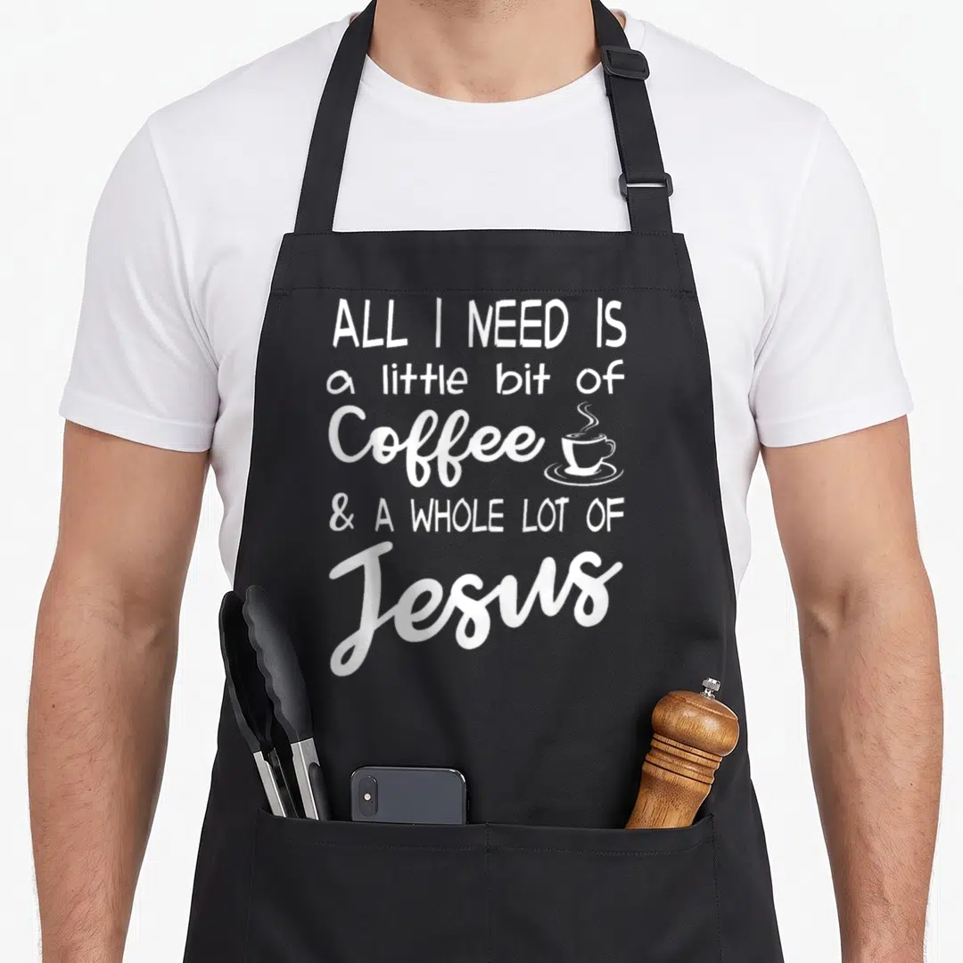 Bit coffee apron - White stacked text reading All I Need Is a Little Bit of Coffee & A Whole Lot of Jesus next — shown on a black cotton canvas apron against a white background