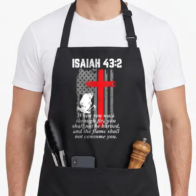 Thin bible verse apron - Red cross over grey flag with kneeling man and Isaiah 43:2 text — shown on a black cotton canvas apron against a white background