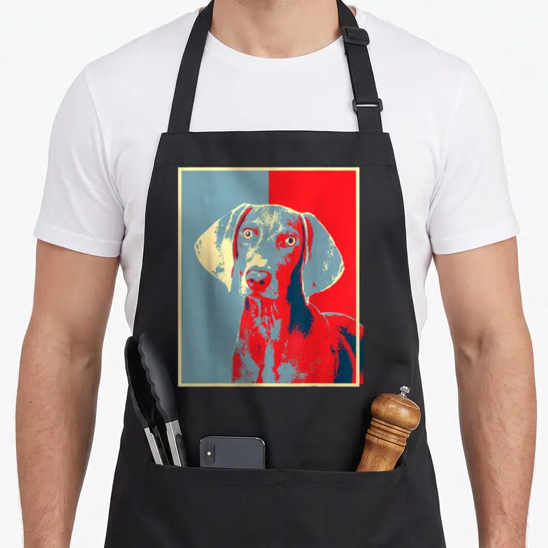 Weim dog apron - Stylized Weimaraner head in red and blue pop art with cream border — shown on a black cotton canvas apron against a white background
