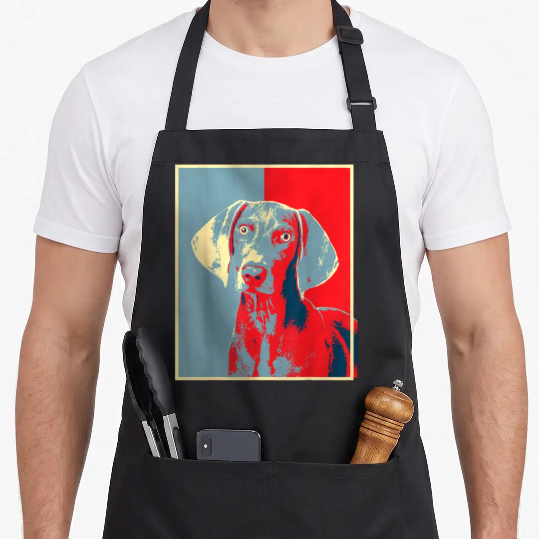 Weim dog apron - Stylized Weimaraner head in red and blue pop art with cream border — shown on a black cotton canvas apron against a white background