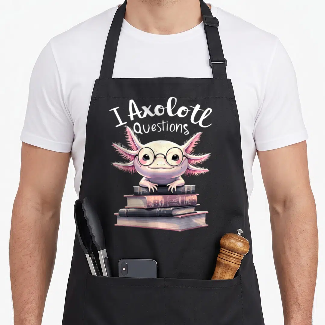 Question anime apron - Cartoon axolotl with glasses resting on four books under text I Axolotl Questions — shown on a black cotton canvas apron against a white background