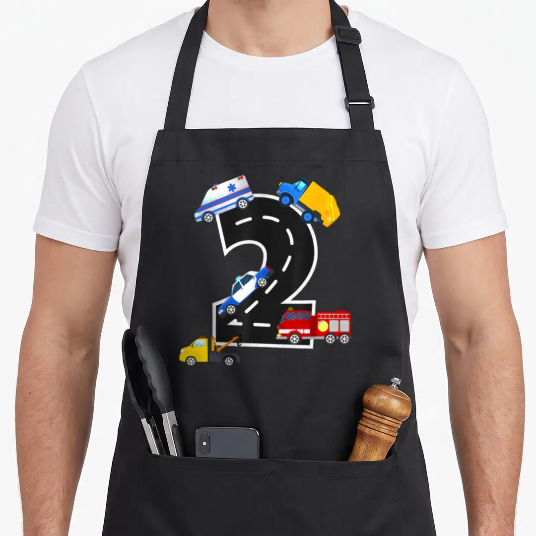 Birthday fire truck apron - Black number 2 road with ambulance, police car, fire truck, tow truck, and garbage truck — shown on a black cotton canvas apron against a white background