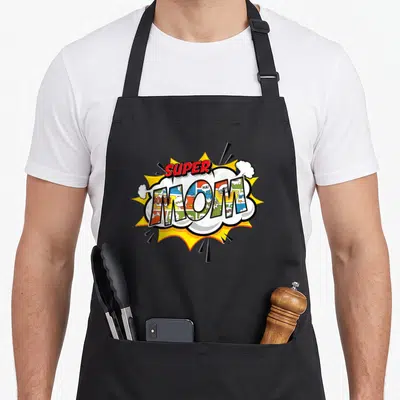 Comic mother's apron - SUPER MOM text in red above comic-panel filled letters inside a white cloud and yellow burst — shown on a black cotton canvas apron against a white background