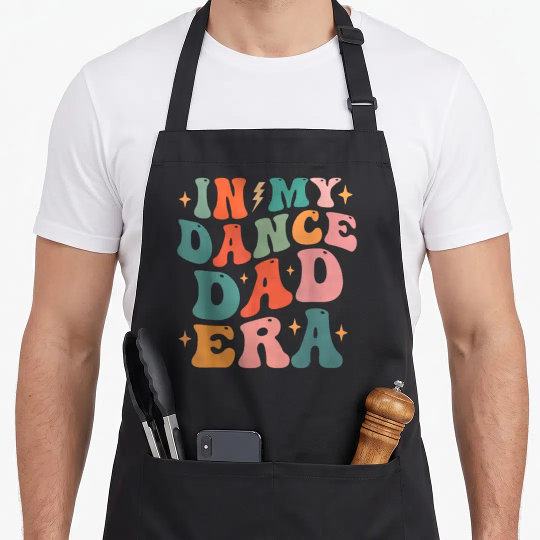 Era dance dad apron - Retro stacked text reading IN MY DANCE DAD ERA in teal, orange, pink, and green with a lightning — shown on a black cotton canvas apron against a white background