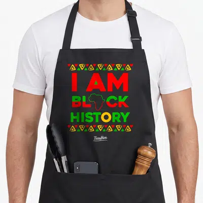 History african american aprons - Stacked I Am Black History text with Africa outline and triangle rows in red green — shown on a black cotton canvas apron against a white background