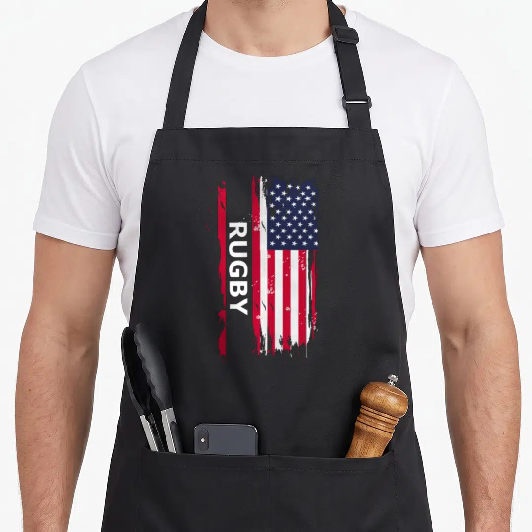 Cute player rugby apron - Vertical RUGBY text over distressed red white and blue USA flag design — shown on a black cotton canvas apron against a white background