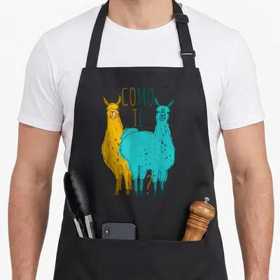 Como spanish aprons - Two llamas yellow and blue with text COMO TE and a question mark — shown on a black cotton canvas apron against a white background