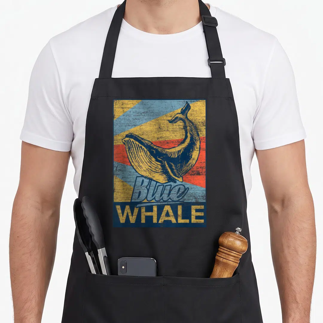 Blue whale animal apron - Retro yellow whale illustration over blue, yellow, and red rays with Blue WHALE text — shown on a black cotton canvas apron against a white background