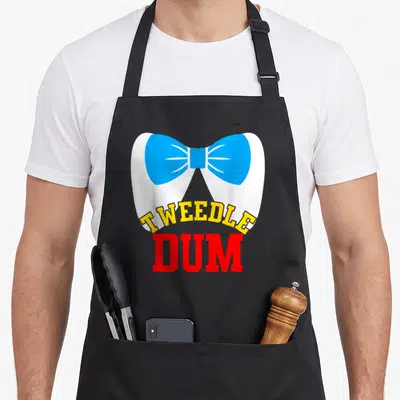 Dee couple apron - Teeth wearing blue bow tie with Tweedle Dum text in yellow and red — shown on a black cotton canvas apron against a white background