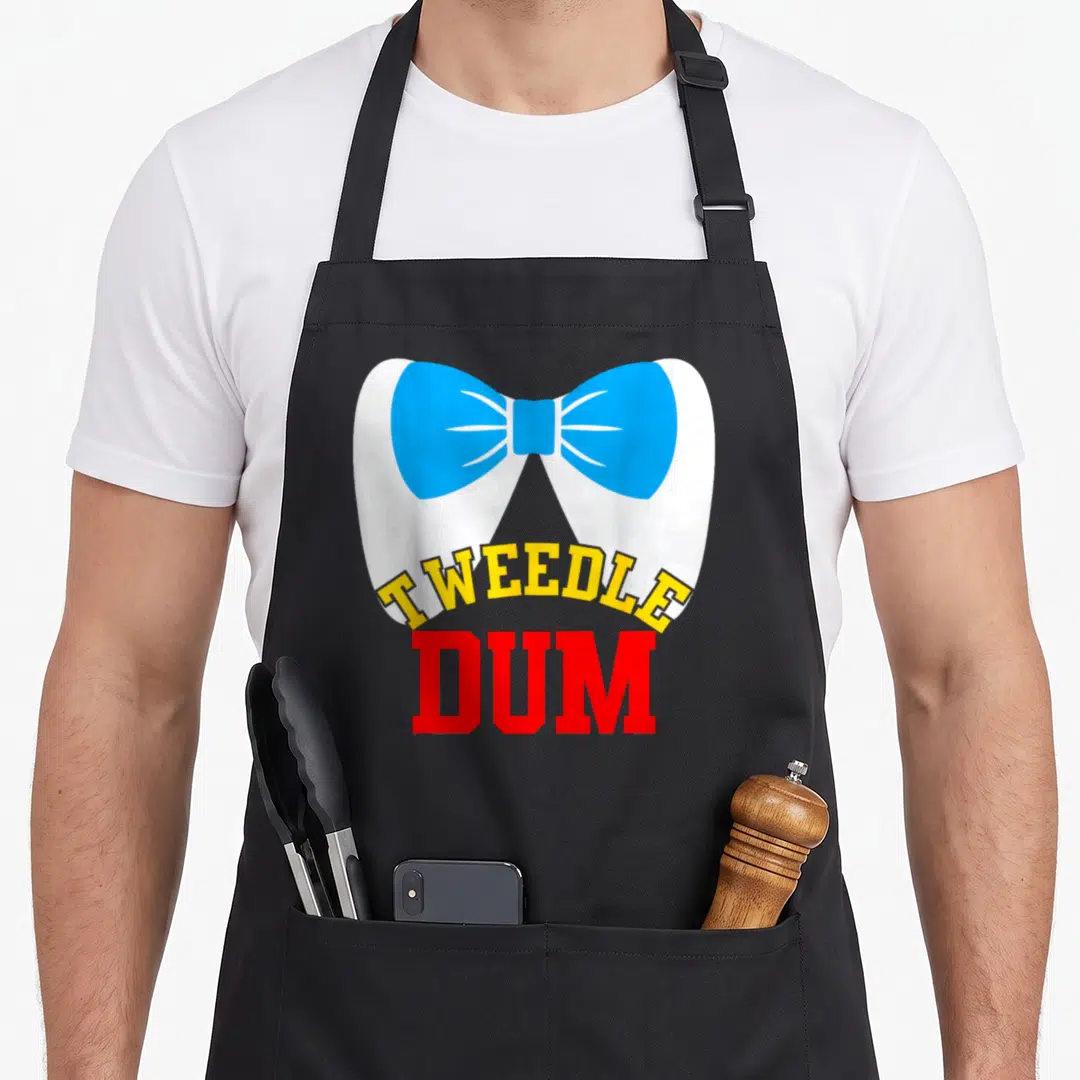 Dee couple apron - Teeth wearing blue bow tie with Tweedle Dum text in yellow and red — shown on a black cotton canvas apron against a white background