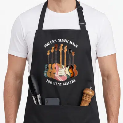 Acoustic crew apron - Seven cartoon guitars in pink blue brown yellow and white with arched white text — shown on a black cotton canvas apron against a white background