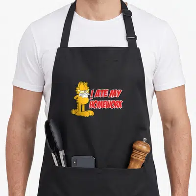 Funny ate homework apron - Orange Garfield holding torn paper next to red I ATE MY HOMEWORK text — shown on a black cotton canvas apron against a white background