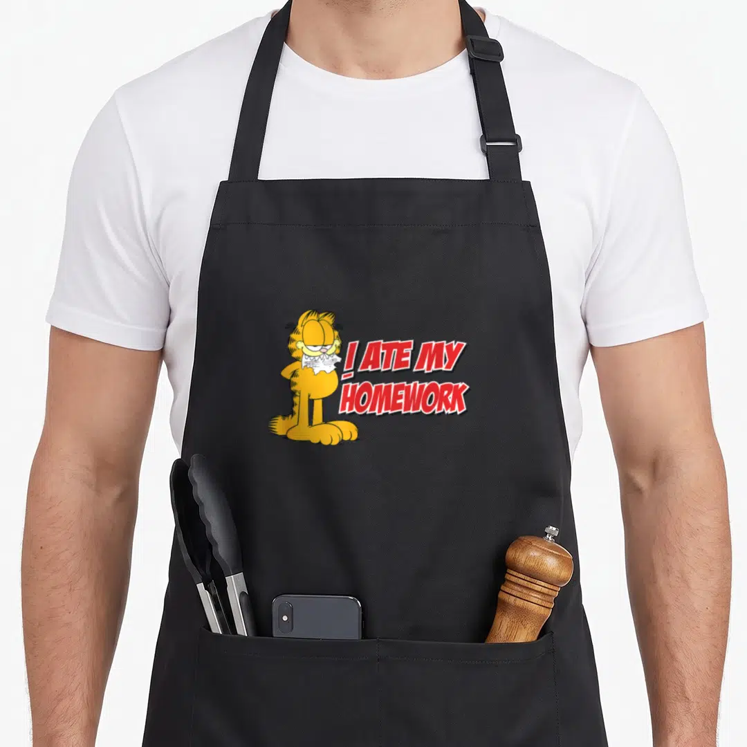 Funny ate homework apron - Orange Garfield holding torn paper next to red I ATE MY HOMEWORK text — shown on a black cotton canvas apron against a white background