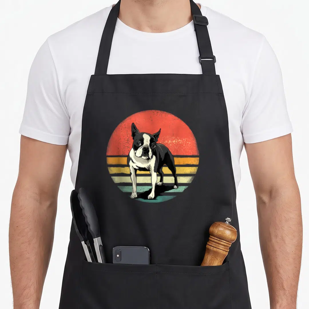 Boston custom pet apron - Retro black and white Boston Terrier dog standing in front of a red orange and yellow striped — shown on a black cotton canvas apron against a white background