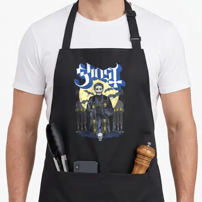 Host ghost apron - Gothic robed man, moon, candles, skull, bat, and GHOST text in blue and yellow — shown on a black cotton canvas apron against a white background