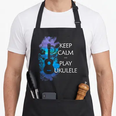 Play ukulele apron - Grey ukulele over blue purple abstract swirls with stacked white text KEEP CALM AND PLAY UKULELE — shown on a black cotton canvas apron against a white background