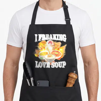 Freaking kitten apron - Cartoon cat head amid flames with three soup bowls and I FREAKING LOVE SOUP text — shown on a black cotton canvas apron against a white background