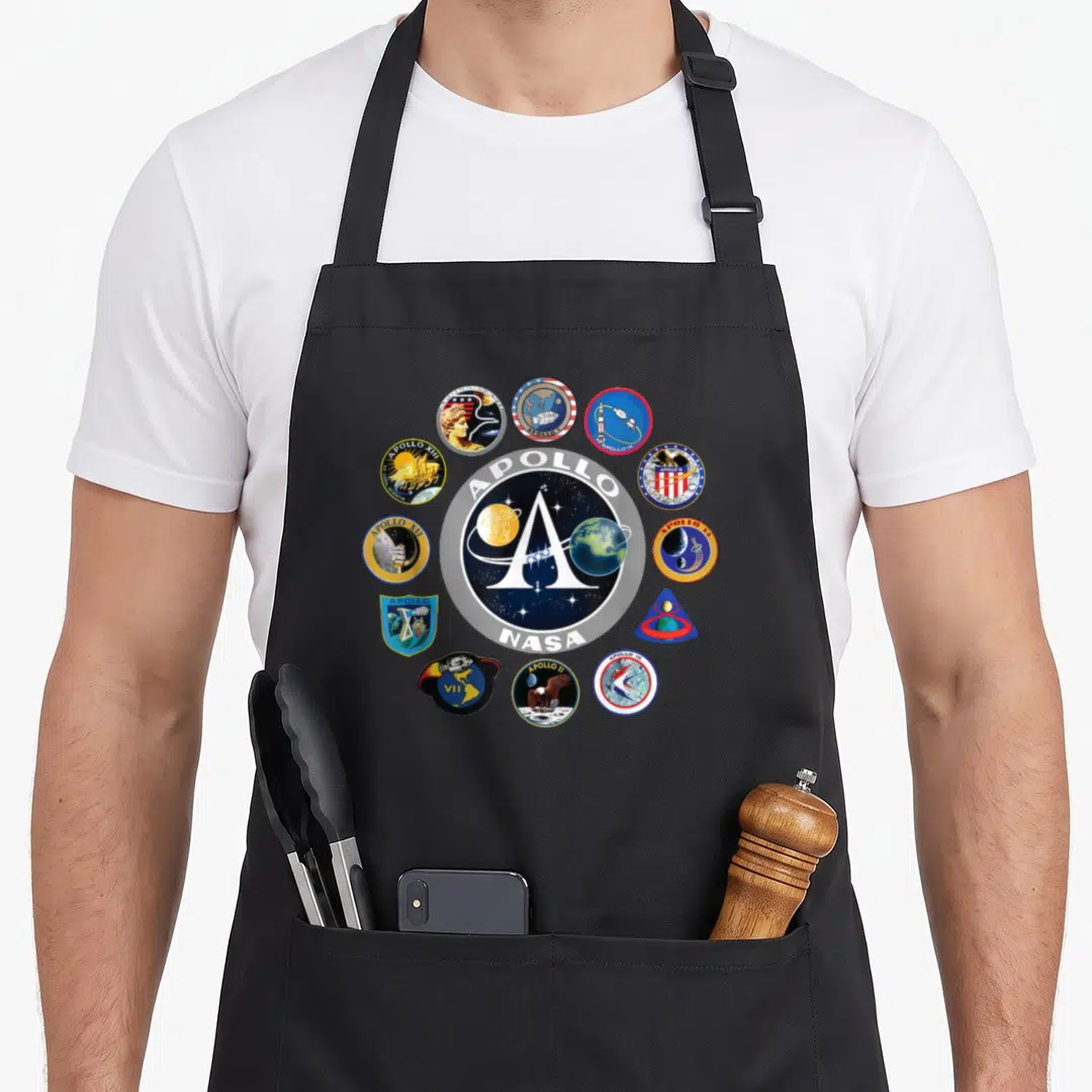 Nasa apollo apron - Circular NASA emblem surrounded by Apollo VII through Apollo XVI mission patches in blue and red — shown on a black cotton canvas apron against a white background