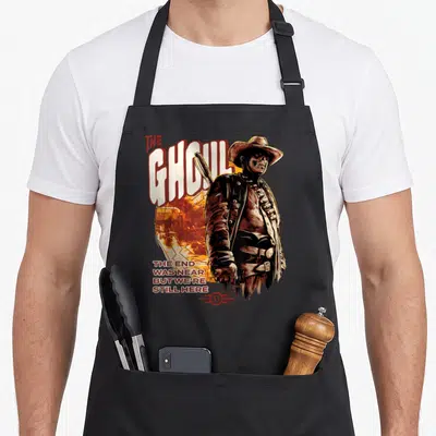 Ghoul modern apron - Western man in hat holding weapon next to THE GHOUL text and orange circle background — shown on a black cotton canvas apron against a white background