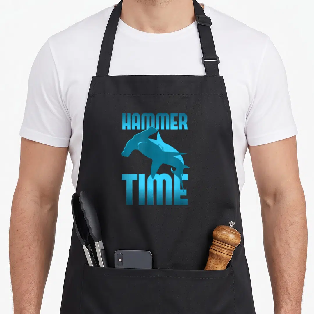 Hammerhead hammer apron - Blue cartoon hammerhead shark between HAMMER and TIME text — shown on a black cotton canvas apron against a white background