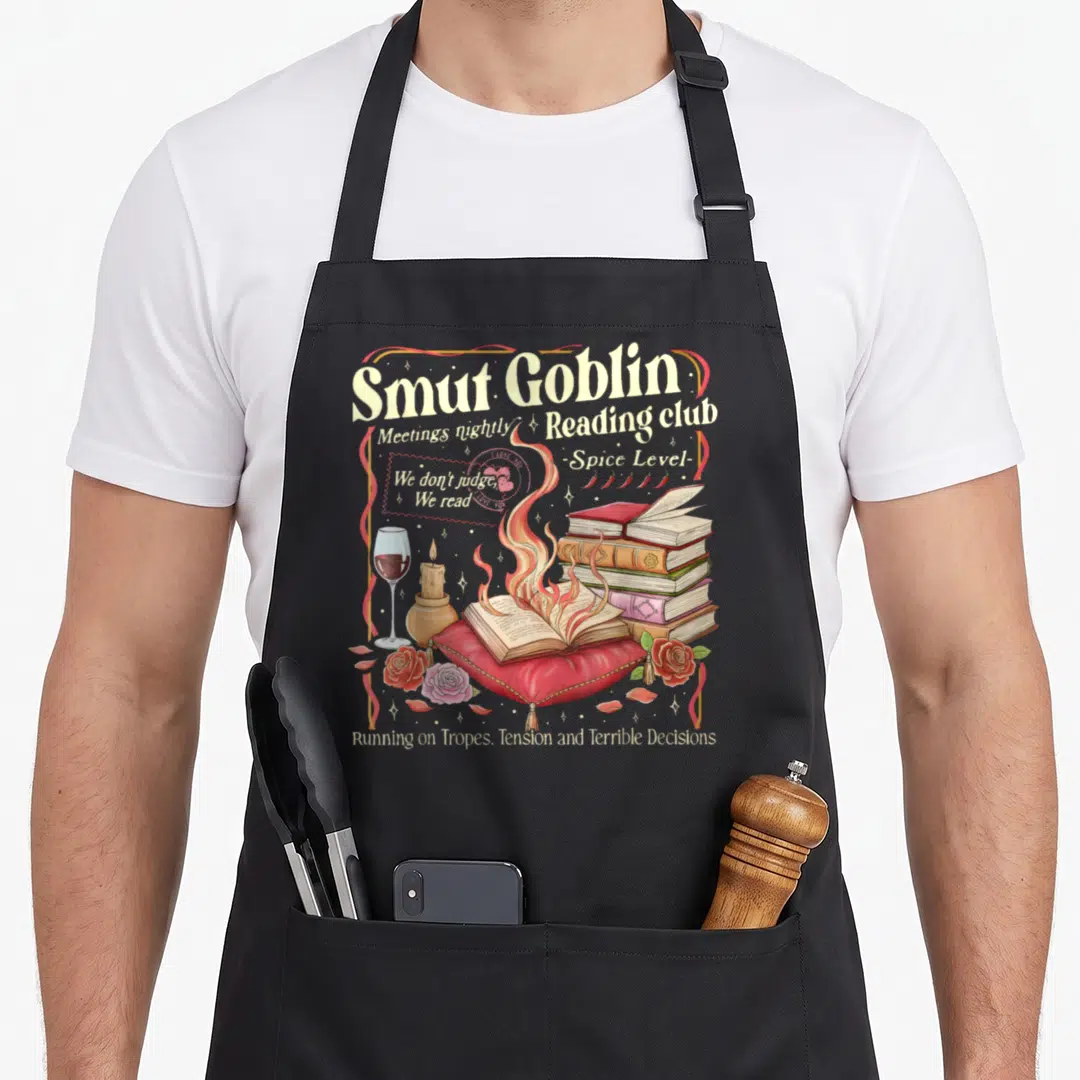 Smut goblin apron - Burning book on red pillow with wine glass and reading club text in vintage style — shown on a black cotton canvas apron against a white background