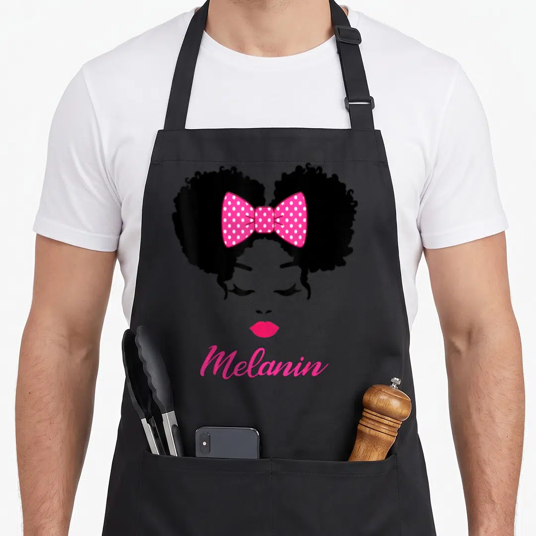 Afro tie apron - Black woman silhouette with pink polka dot bow and Melanin text — shown on a black cotton canvas apron against a white background