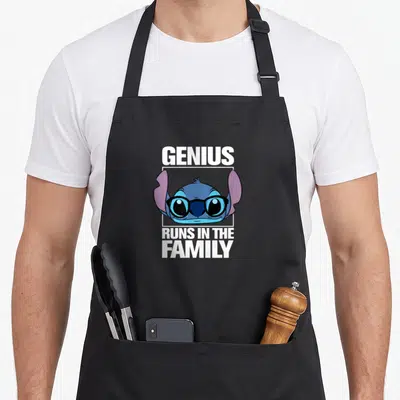 Funny genius apron - Stitch head wearing glasses with GENIUS RUNS IN THE FAMILY text — shown on a black cotton canvas apron against a white background