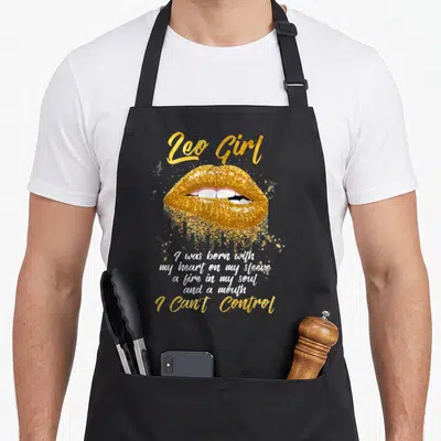 Funny leo birthday apron - Gold glittery lips with white script text and Leo Girl lettering — shown on a black cotton canvas apron against a white background