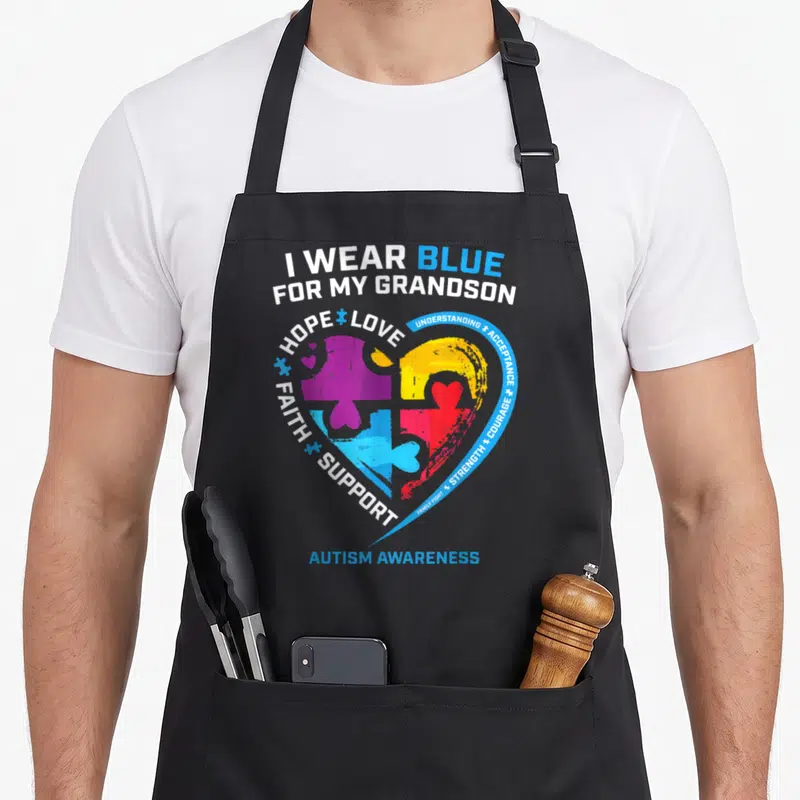 Blue grandparent apron - Heart of puzzle pieces in blue purple yellow red with text I wear blue for my grandson autism — shown on a black cotton canvas apron against a white background