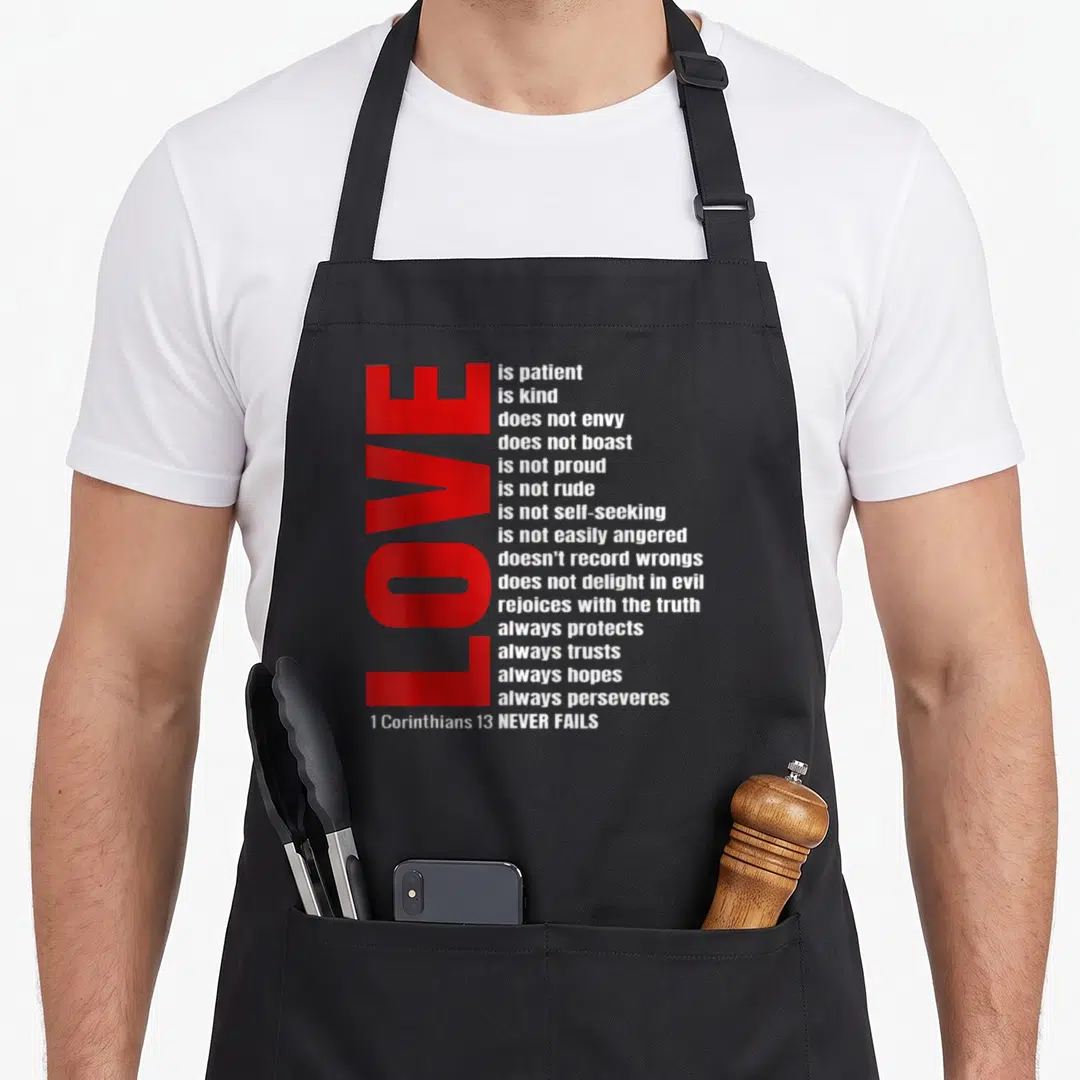 Patient bible verse apron - Vertical red LOVE next to 17 lines of white scripture text from 1 Corinthians 13 — shown on a black cotton canvas apron against a white background