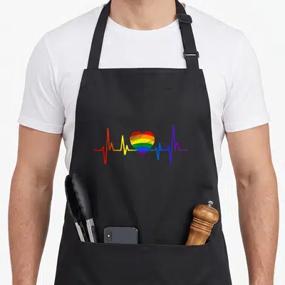Lovely gay pride apron - Rainbow heart on heartbeat line with red orange yellow green blue purple stripes — shown on a black cotton canvas apron against a white background