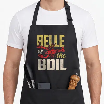 Cajun crawfish boil apron - Red lobster illustration with Belle of the Boil text in yellow and white distressed fonts — shown on a black cotton canvas apron against a white background
