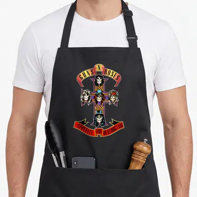 Vintage rose gun apron - GUNS N ROSES cross with four skeleton heads and APPETITE FOR DESTRUCTION banner in red yellow — shown on a black cotton canvas apron against a white background